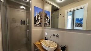 Ein modernes Badezimmer mit einer gläsernen Duschkabine, einem beige gefärbten Steintonne und einem hölzernen Waschtisch.
