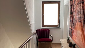 A narrow stairway with a wooden handrail, a red upholstered chair, a small table with potted plants, and a window with a view of the outside. - Holiday Home with Private Bar and Sauna (Duderstadt)