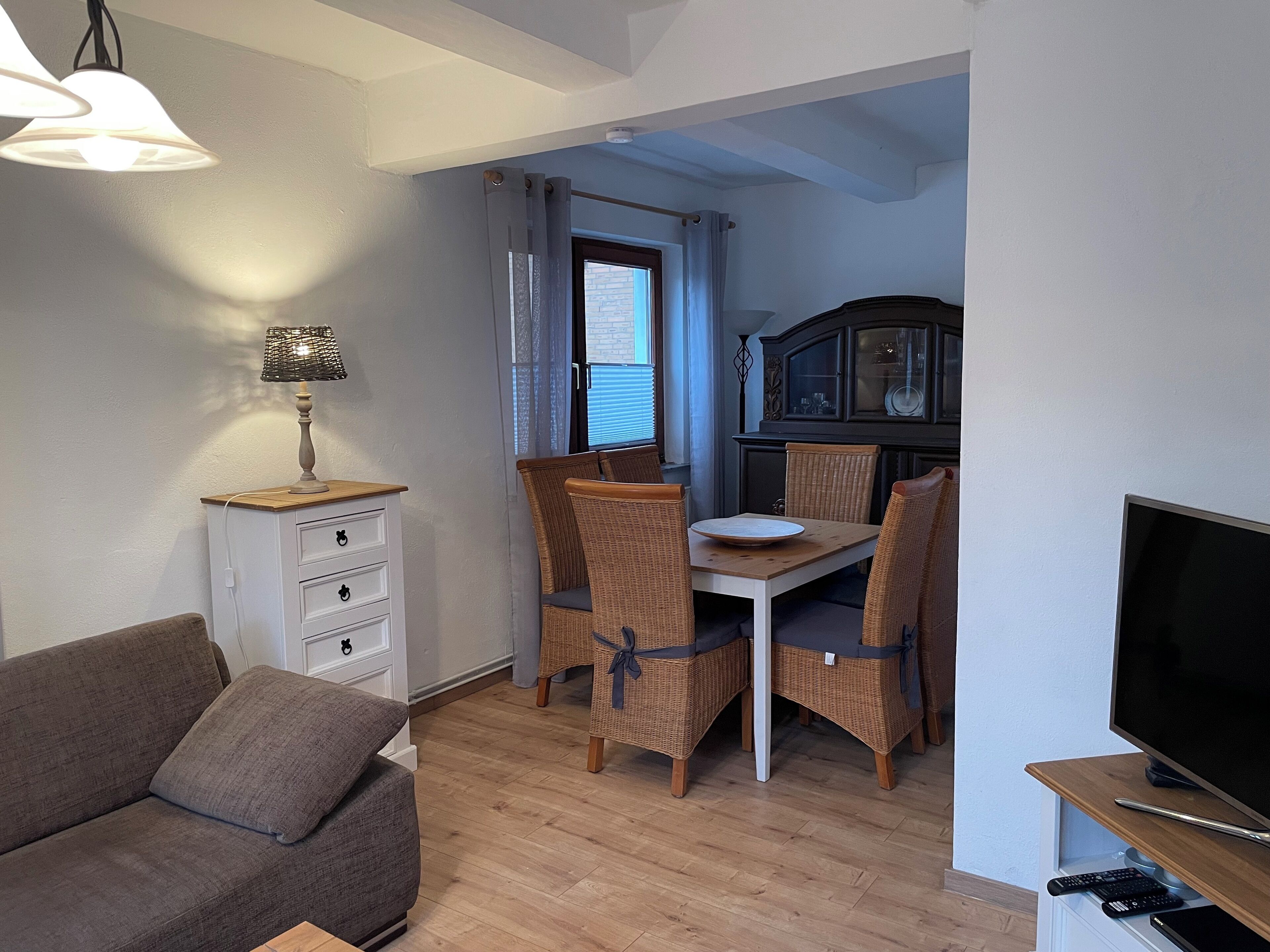 Un salon comprenant un canapé, une table à manger avec des chaises, un téléviseur et un meuble avec des portes en verre.