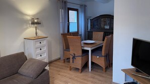A living room with a sofa, a dining table with chairs, a TV, and a cabinet with glass doors. - Holiday Home with Private Bar and Sauna (Duderstadt)