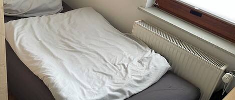 A small, single-bed room with a window, a radiator, and a wooden table.