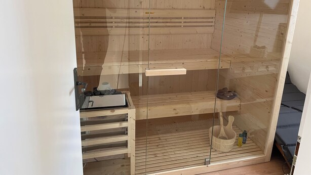 A sauna with wooden walls and a glass door, a control panel, and a bench. - Holiday Home with Private Bar and Sauna (Duderstadt)