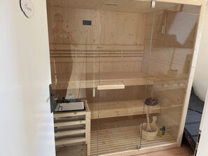 A sauna with wooden walls and a glass door, a control panel, and a bench.