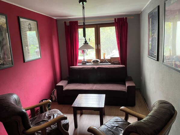 A cozy living room with a red wall, a brown sofa, a wooden coffee table, and two leather chairs.