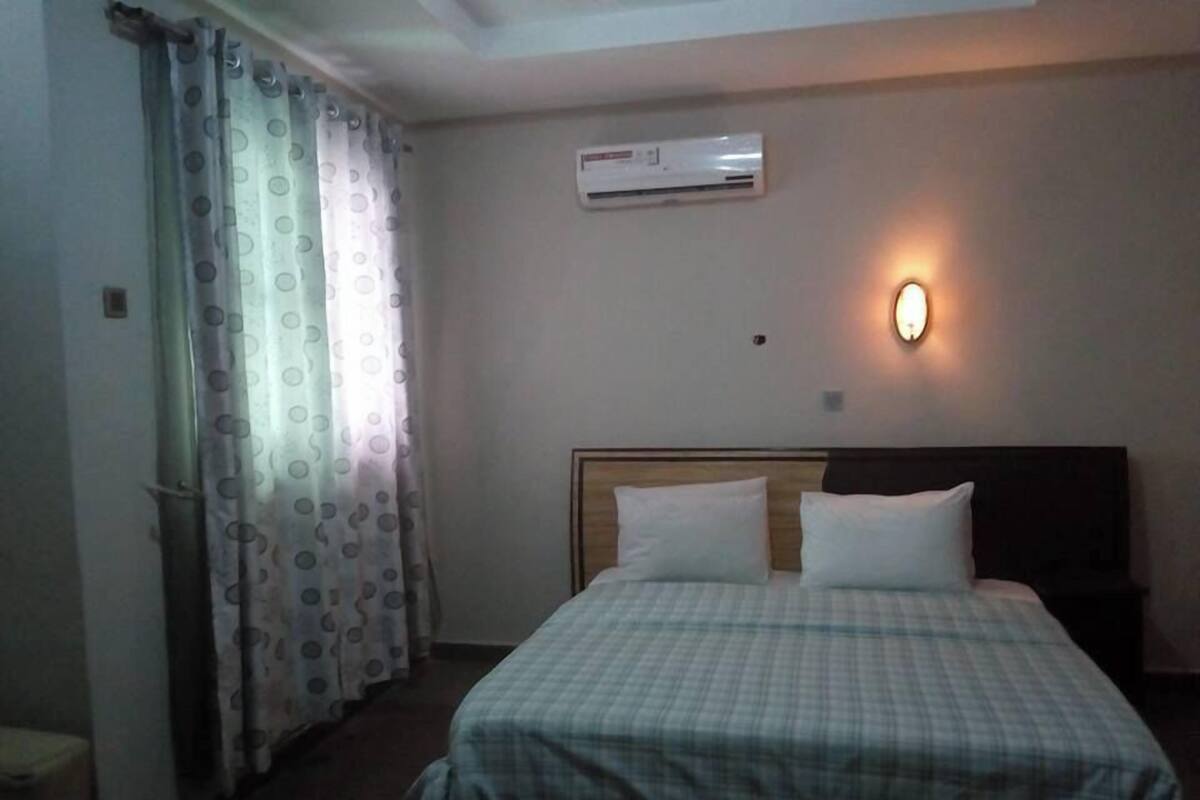 Una habitación de hotel con cama, aire acondicionado de pared y lámpara de pared.