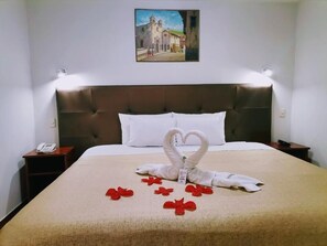 A hotel room with a large bed, a headboard, a painting on the wall, and a phone on the nightstand. - Hotel Urpi (Cusco)