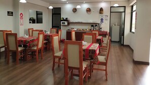 Ένας χώρος τραπεζαρίας με ξύλινα καθίσματα και τραπέζια, μια κουζίνα με φούρνο μικροκυμάτων και καφετι έρα, καθώς και ένα ψυγείο.