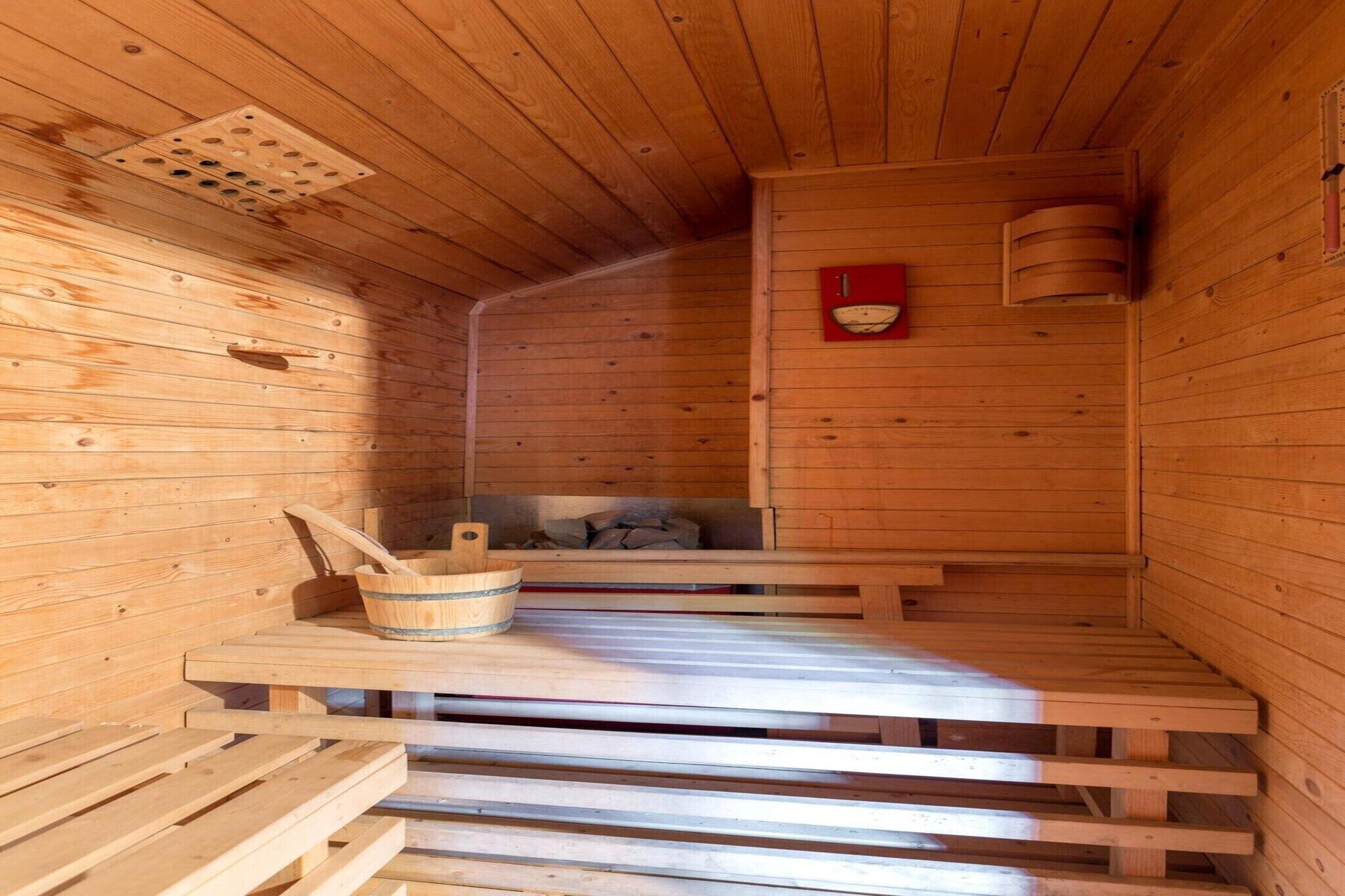 Eine Holzsauna mit Bänken, einem Holzeimer und einem roten Ofen.