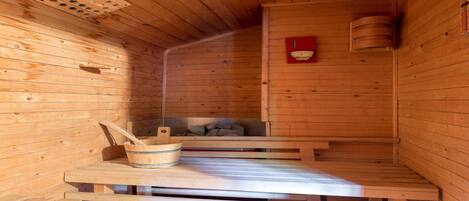 Una sauna de madera con bancos, un cubo de madera y un calentador rojo.