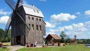A rustic wooden windmill with a metal roof, a wooden barn, and a small wooden structure with a thatched roof.