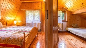 A cozy, wooden-paneled room with a bed, a small table with a lamp, and a window with lace curtains.