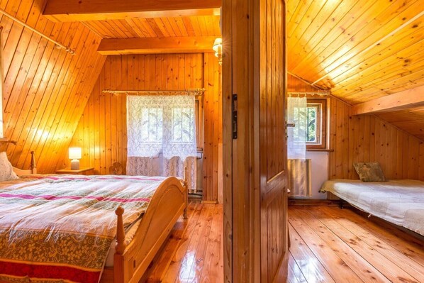 A cozy, wooden-paneled room with a bed, a small table with a lamp, and a window with lace curtains.