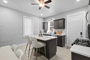 Une cuisine moderne dotée d’un îlot central, de tabourets de bar et de meubles de rangement aux couleurs sombres.
