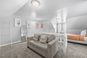 Une chambre avec un plafond en pente, un lit blanc, un canapé gris et un petit bureau.