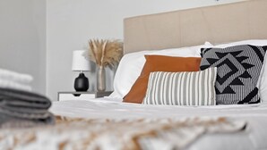 Ein ordentlich bezogenes Bett mit weißen und gestreiften Kissen, einer beigen Kopfteil und einem Nachttisch mit Lampe und Dekoration.