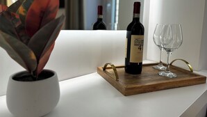 A bottle of wine on a wooden tray with two glasses on a white table, next to a potted plant. - Suites Pantheon Rome - 3 (Roma)
