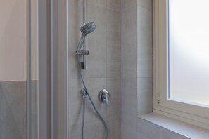 Eine Dusche mit Handbrause und Wandarmatur in einem gefliesten Badezimmer.
