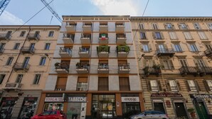 A multi-story building with balconies, storefronts including a tobacconist and a pastry shop, and parked cars on the street. - Casa Fiore by Wonderful Italy (Turin)