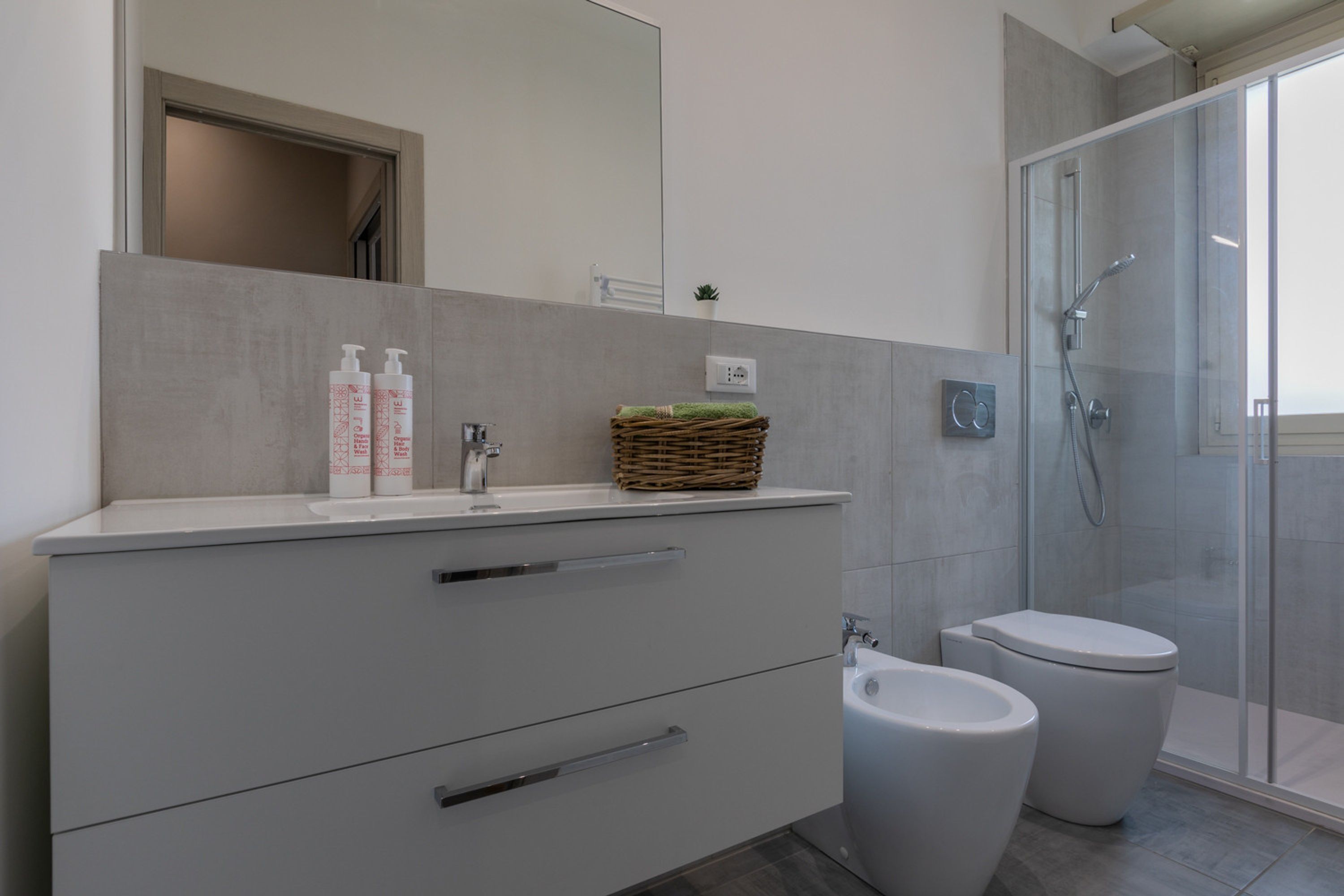 Ein modernes Badezimmer mit einem weißen Waschtisch, zwei weißen Toiletten, einer Duschkabine aus Glas und einem kleinen Blumentopf auf dem Waschtisch.