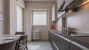 A modern kitchen with a built-in stove, a window with blinds, and a dining area with chairs and a table. - Casa Fiore by Wonderful Italy (Turin)