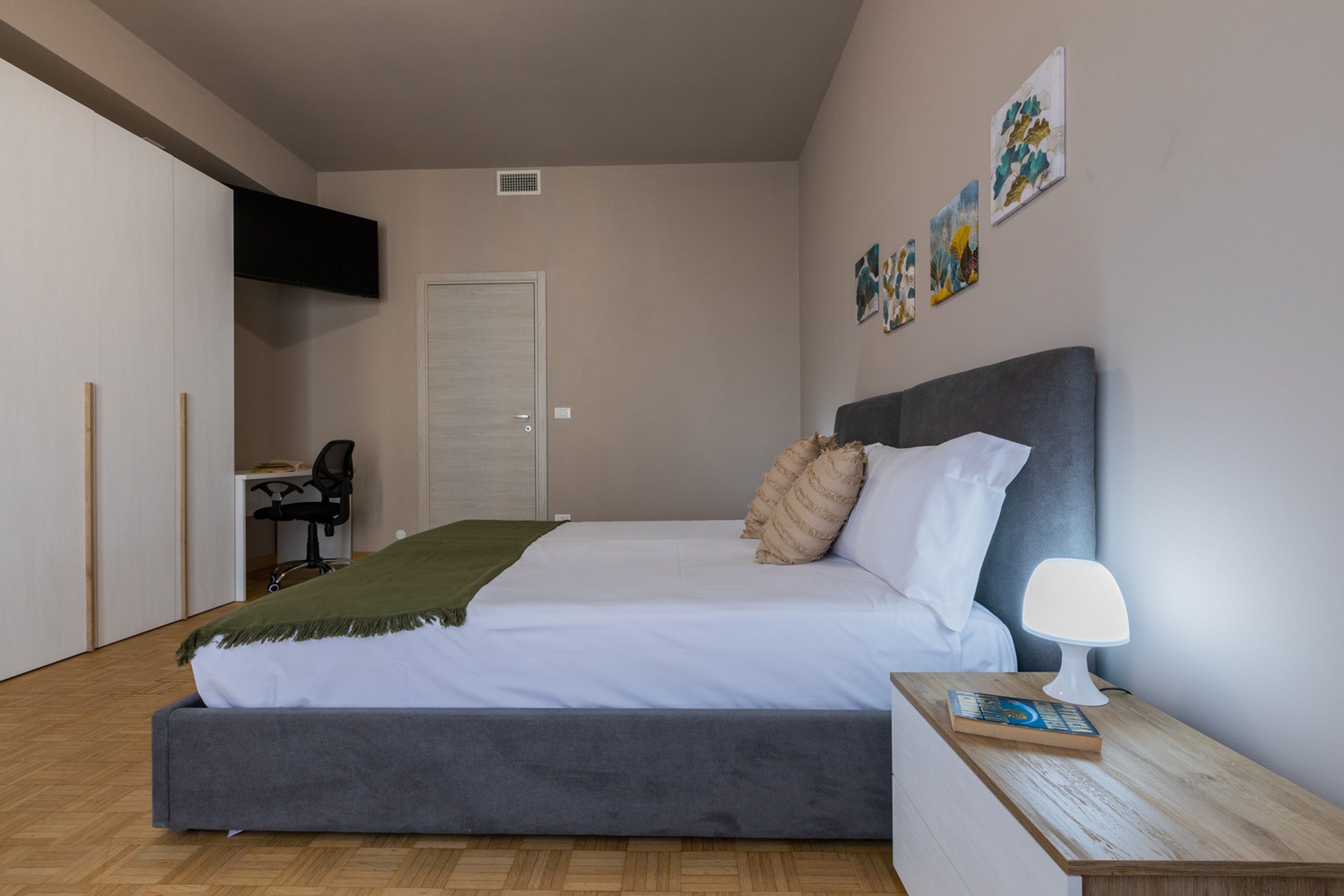Un dormitorio con cama, mesita de noche, lámpara y una obra de arte en la pared.