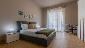 Ein Schlafzimmer mit Bett, Nachttisch, Lampe, Kunstwerk und Blick ins Freie.