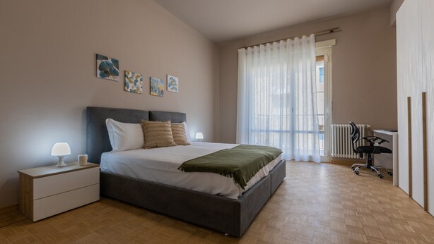 A bedroom with a bed, nightstand, lamp, artwork, and a view of the outdoors. - Casa Fiore by Wonderful Italy (Turin)