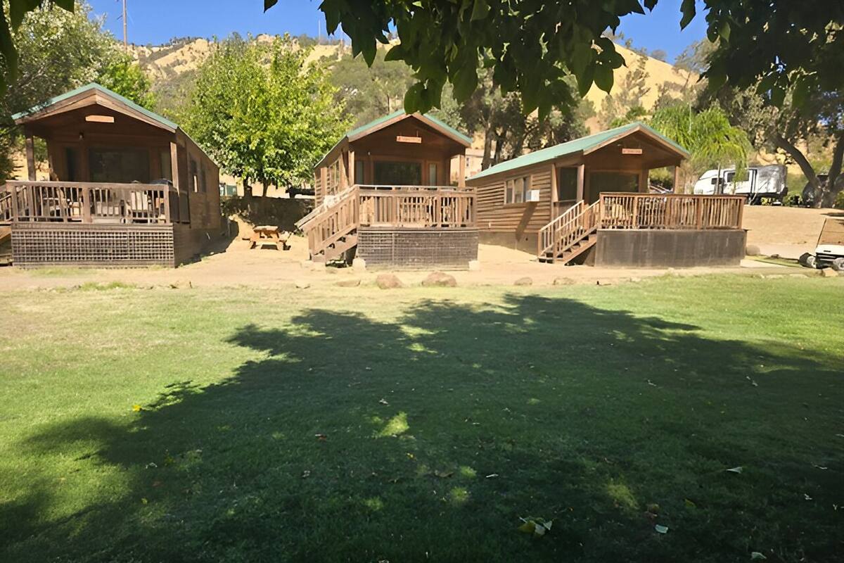 A campground with three wooden cabins, each with a balcony and a small deck.