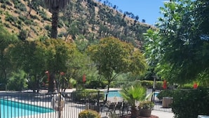 A pool area with a fenced pool, surrounded by various plants and trees, with a hillside in the background. - Canyon Creek Resort (Winters)