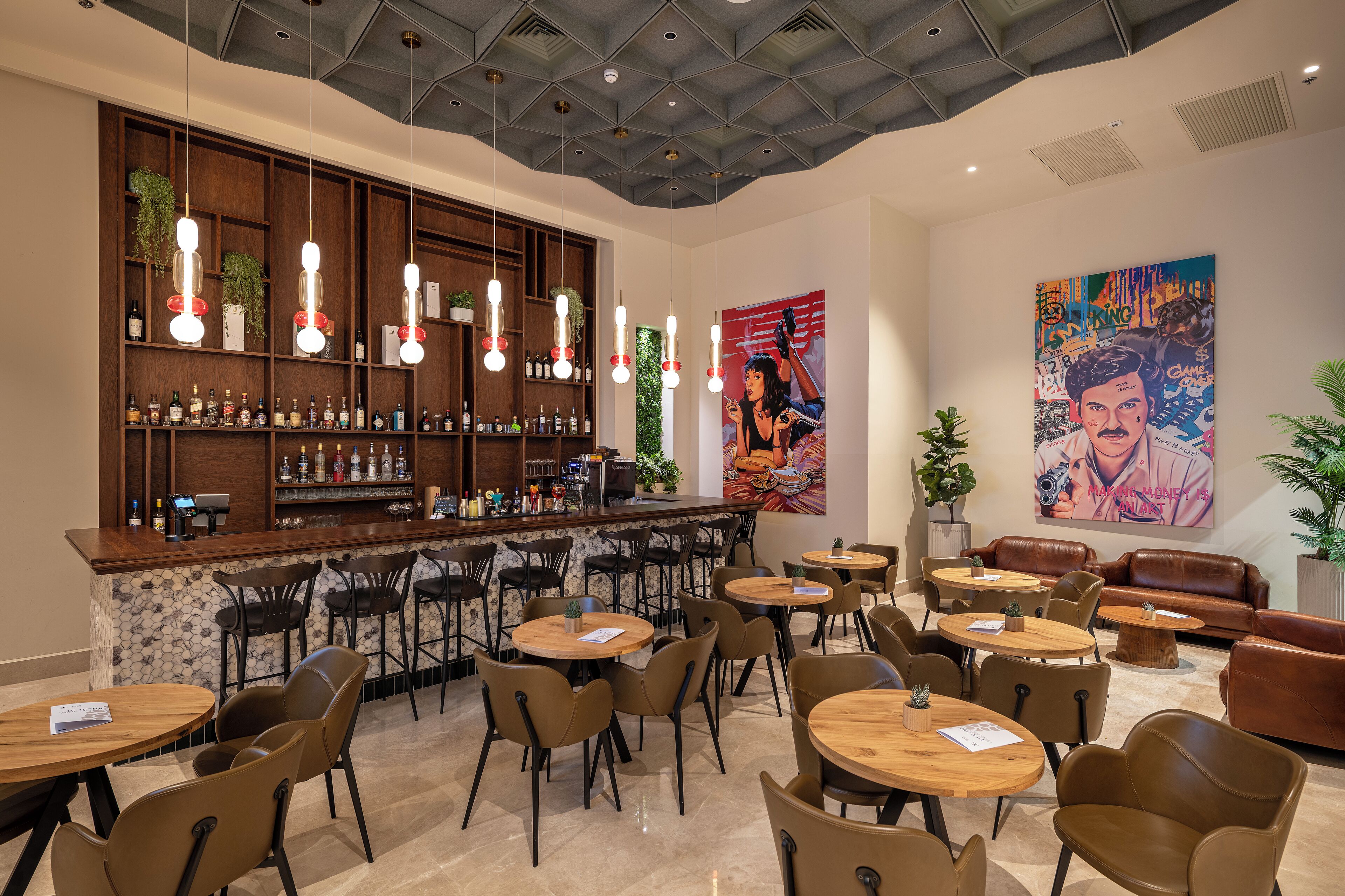 A modern bar area with a wooden counter, multiple seating options including round tables and chairs, and a ceiling with a geometric pattern.