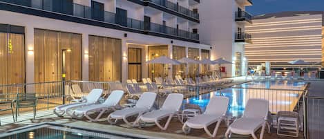 Una piscina al aire libre, sombrillas, sillones reclinables de piscina