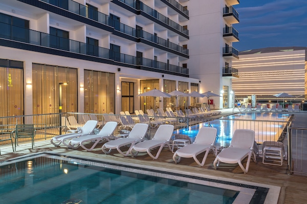 Una piscina al aire libre, sombrillas, sillones reclinables de piscina