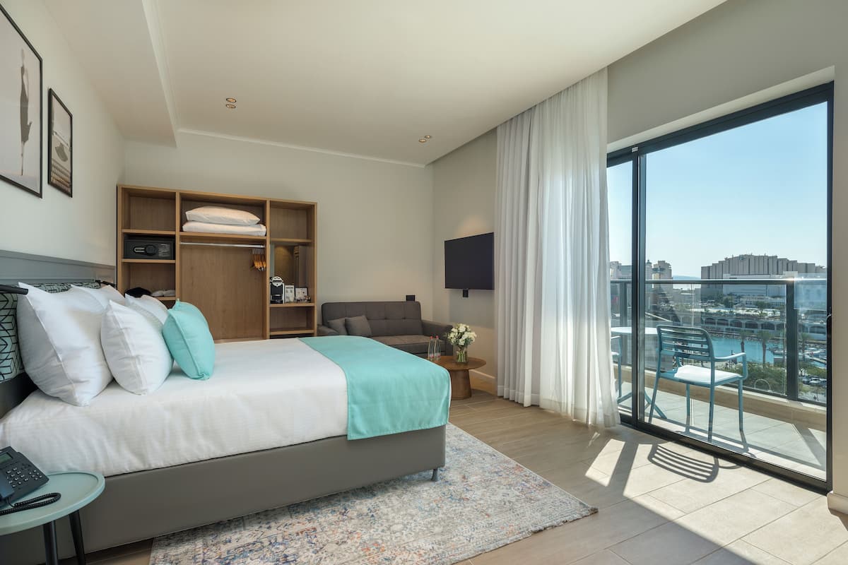 A modern hotel room with a large bed, a TV, a balcony with a view, and a wooden wardrobe.