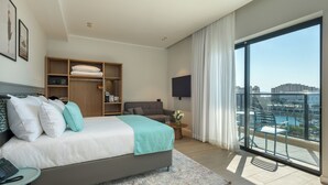 A modern hotel room with a large bed, a TV, a balcony with a view, and a wooden wardrobe.