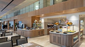 A modern hotel lobby with a central food station, seating areas, and a glass-enclosed upper level.