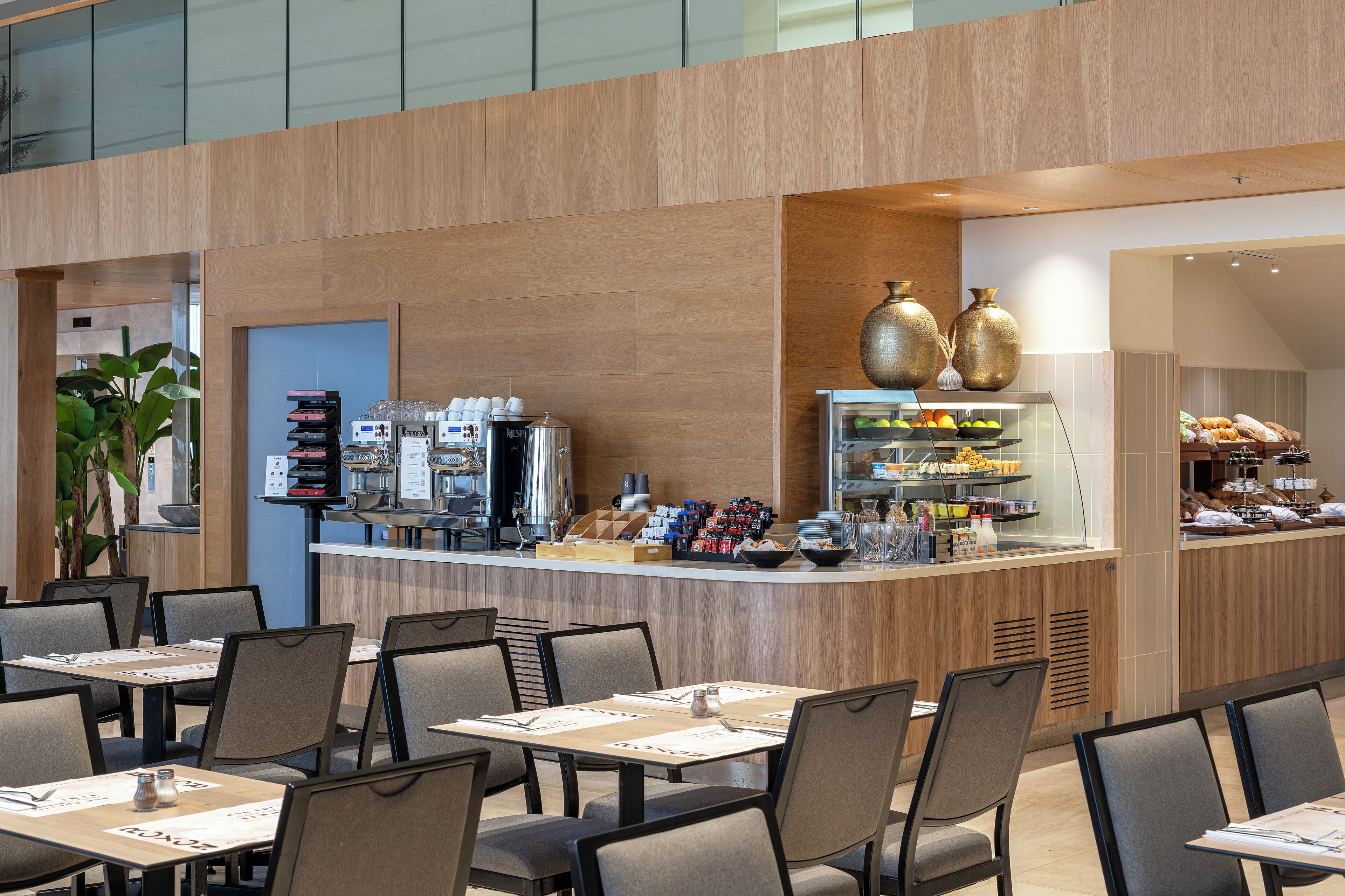 A modern cafe with a wooden counter, seating area, and a variety of food and drink options.