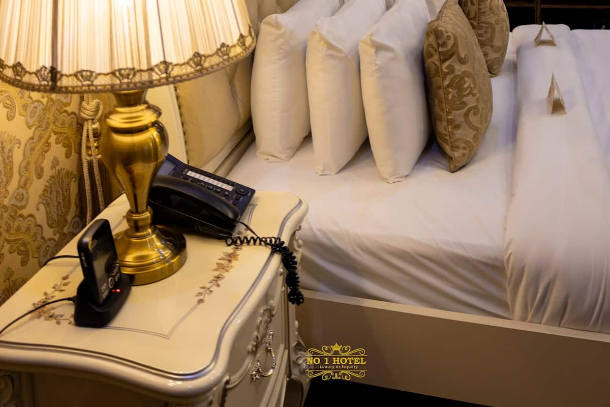 A luxurious hotel room with an ornate bed, two bedside lamps, a telephone, and a decorative wall.