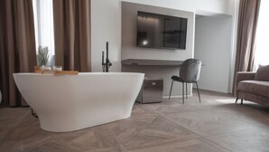 A modern bathroom with a freestanding bathtub, a vanity with a mirror, and a flat-screen TV mounted above the mirror. - Alexander House Hotel  (San Ferdinando)