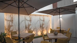A dining area with marble walls, yellow chairs, and large umbrellas. - Alexander House Hotel  (San Ferdinando)