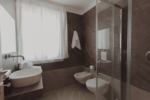Casa de banho moderna com uma grande lavatório oval, um bidé e uma cabine de duche de vidro.