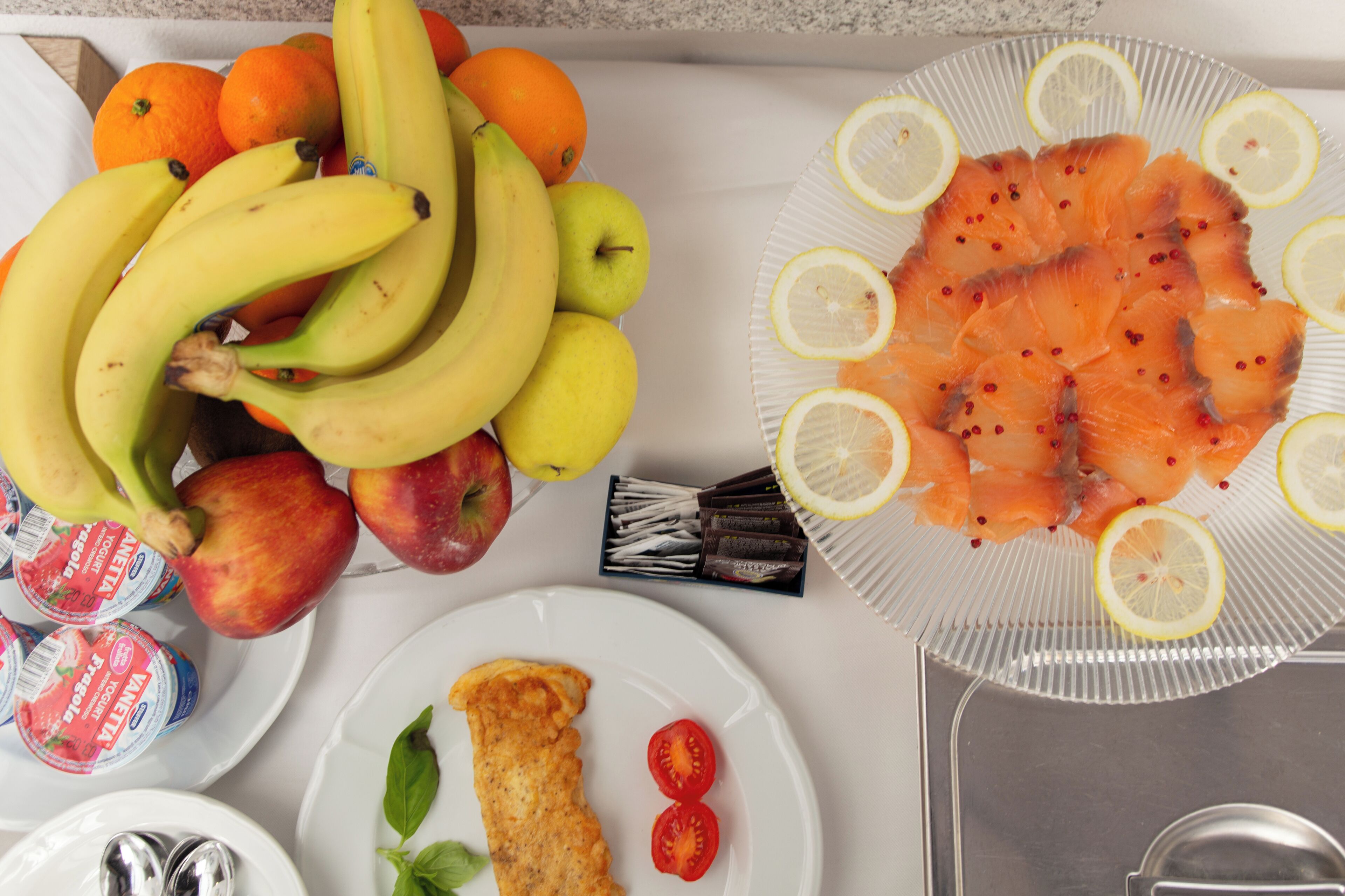 Una mesa con diversos alimentos, como plátanos, manzanas, tomates y lonchas de salmón.