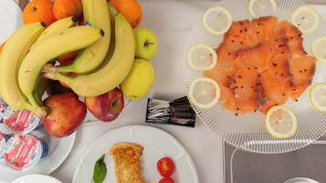 Una mesa con diversos alimentos, como plátanos, manzanas, tomates y lonchas de salmón.