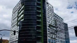 Un immeuble à plusieurs étages doté d’une façade incurvée, de grandes fenêtres et d’un mélange de balcons et de terrasses.