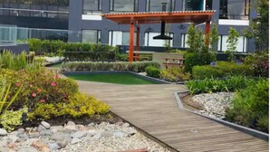 Un bâtiment moderne doté d’une terrasse en bois, entouré de jardins aménagés et offrant une vue sur les montagnes.