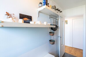 Kitchen area with a door, featuring a decorative shelf, woven baskets, and a small storage space.