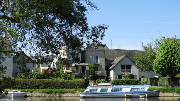 A canal with a houseboat docked near the shore, surrounded by lush greenery and a clear sky. - Camping du Lion d'Angers (Le Lion-d'Angers)