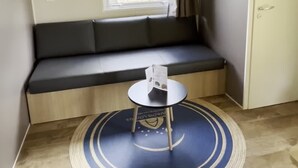 A small room with a window, a sofa, a small table, and a door. - Camping du Lion d'Angers (Le Lion-d'Angers)