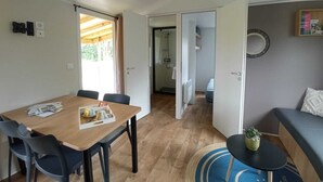 A room with a wooden dining table, chairs, a sofa, a small round table with a plant, and a door leading to a bathroom. - Camping du Lion d'Angers (Le Lion-d'Angers)