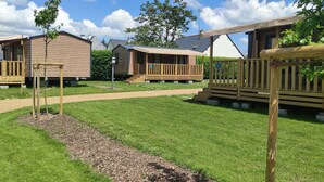 A row of wooden cabins with a grassy lawn and a pathway. - Camping du Lion d'Angers (Le Lion-d'Angers)