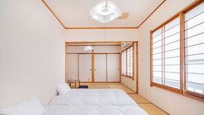 Een traditionele Japanse slaapkamer met tatami vloerbedekking, een futonbed, schuifdeuren en een groot raam met shoji schermen.